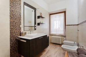 Ein modernes Badezimmer mit einem großen Spiegel, einem weißen Waschbecken, dunklen Holzschränken und einem Bidet.