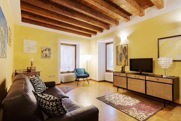 Ein Wohnzimmer mit einem braunen Ledersofa, einem blauen Sessel, einem Holzschrank und einem Fernseher.
