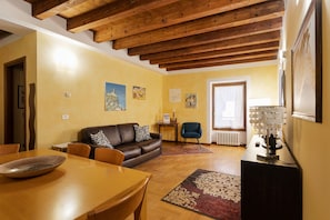 Ein Wohnzimmer mit Holzboden, einem braunen Ledersofa, einem Esstisch mit Stühlen und einer TV-Konsole mit einer Lampe.
