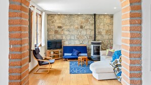 A cozy living room with a stone wall, a fireplace, a sofa, a chair, and a television.