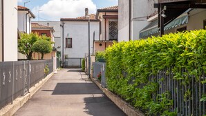 A narrow street flanked by residential buildings with a metal fence and greenery on one side.