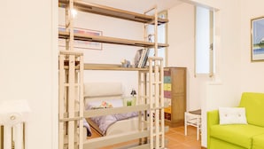 A bunk bed with a ladder, a small table, a green armchair, and a cabinet with multiple drawers. - Torre dell'Orologio Apartment (Padova)