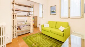 A room with a bunk bed, a green sofa, a small table, and a window with curtains. - Torre dell'Orologio Apartment (Padova)