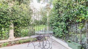 A round metal table with a glass top, surrounded by a wrought iron fence and lush greenery. - Torre dell'Orologio Apartment (Padova)