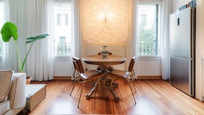 A dining area with a round table, four chairs, a potted plant, a suitcase, and a refrigerator. - Scrovegni Design Apartment (Padova)