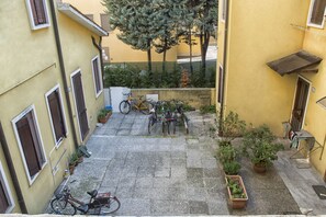 A courtyard with bicycles parked, potted plants, and a building with yellow walls and brown shutters. - Piazza dei Frutti Flat (Padova)