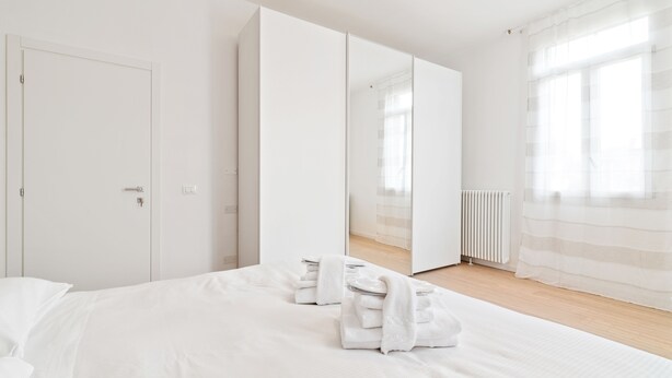Une chambre à coucher moderne avec un grand lit, une armoire et un miroir.