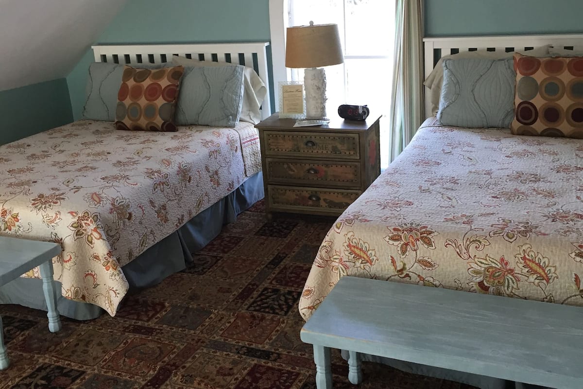 A bedroom with two beds, a nightstand, a window with curtains, and a patterned carpet.