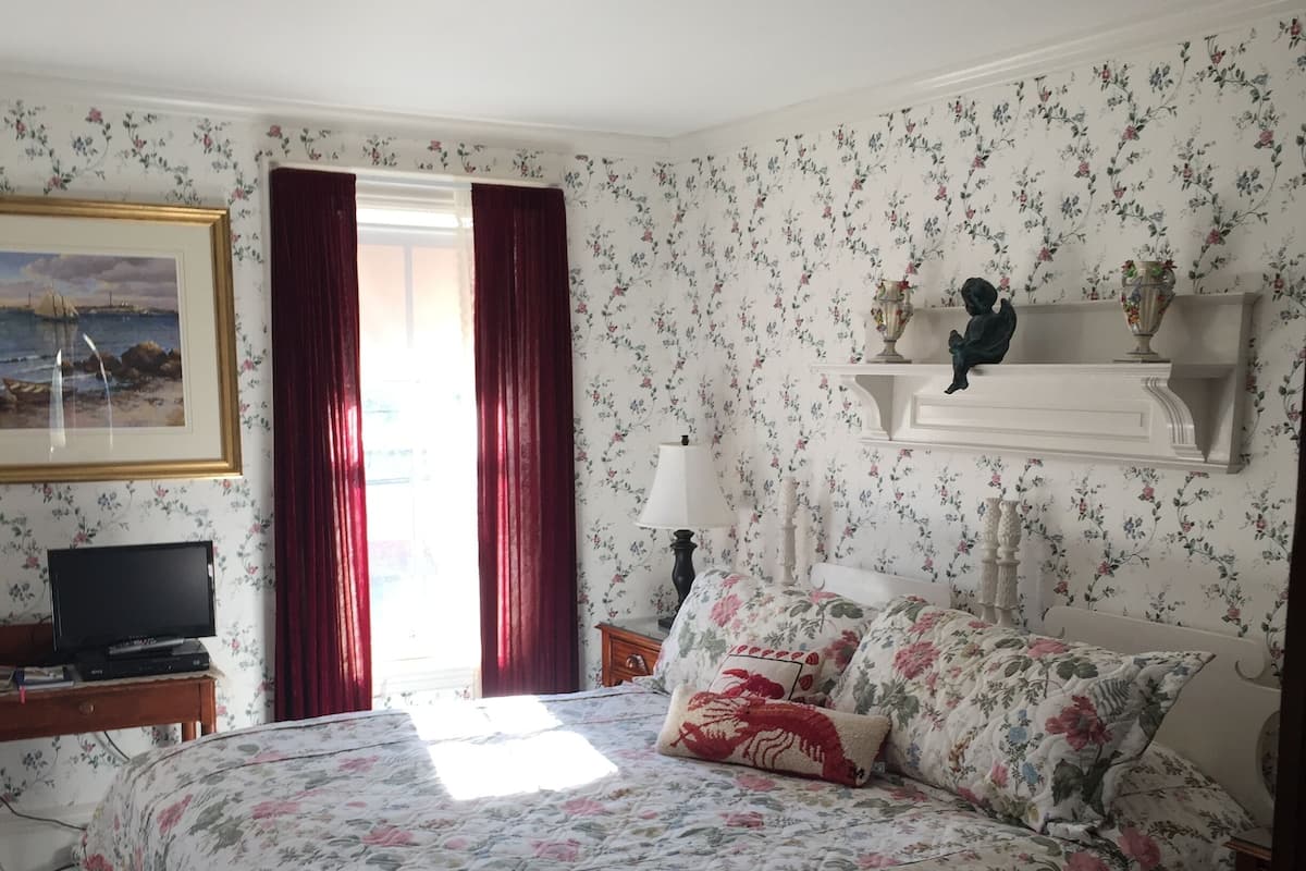 A bedroom with a floral bedspread, a television on a wooden table, and a framed picture on the wall.