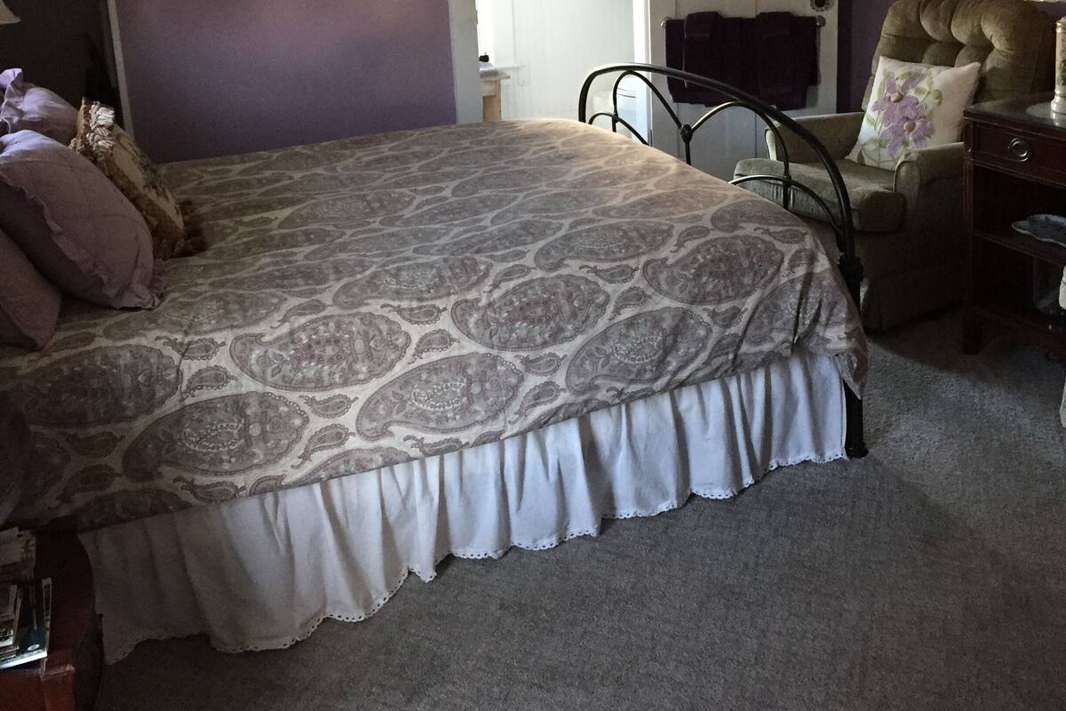 A bedroom with a large bed, a chair, a nightstand, and a door leading to another room.