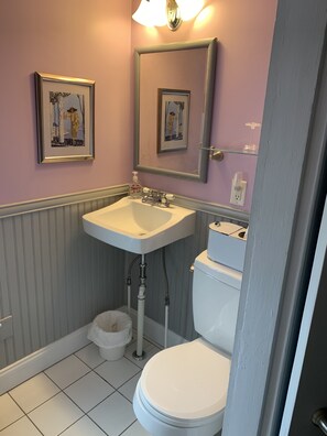 A bathroom with a white sink, a toilet, and two framed pictures on the wall. - Lantana House (Rockport)