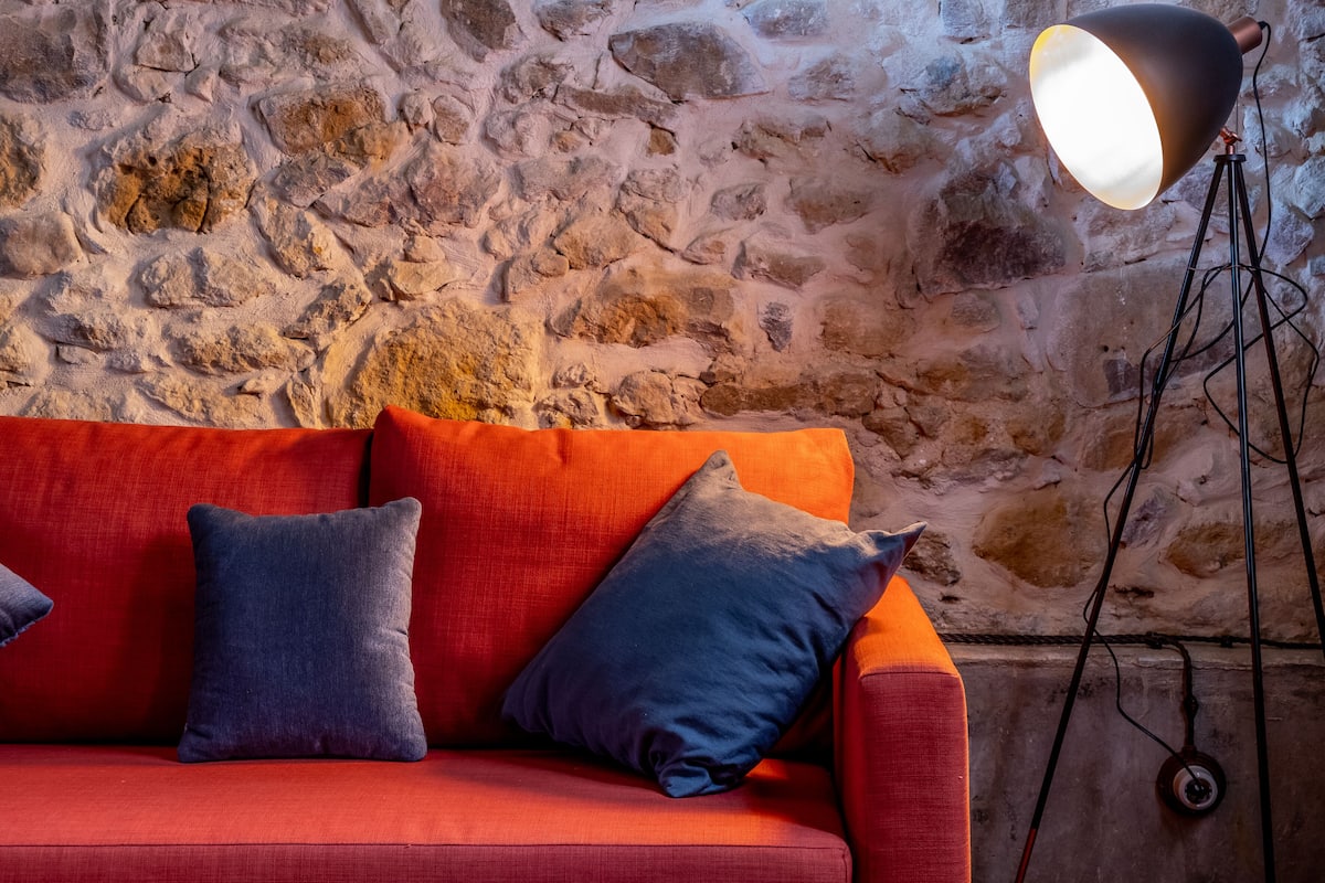 A red sofa with two pillows against a stone wall.
