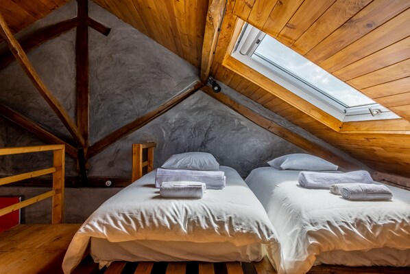 Un dormitorio acogedor en el ático con dos camas, un tragaluz y techo de madera.