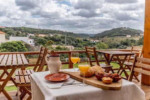 A wooden deck with a table set for breakfast, including a jug, glasses of orange juice, bread, and pastries. - Terra Lodge (Mafra)