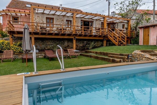 A swimming pool with a wooden deck, a stone building with a wooden deck and stairs, and a small shed. - Terra Lodge (Mafra)