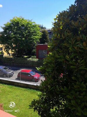 A parking area with a red car, a metal fence, and greenery. - Flatmilan (Cernusco sul Naviglio)