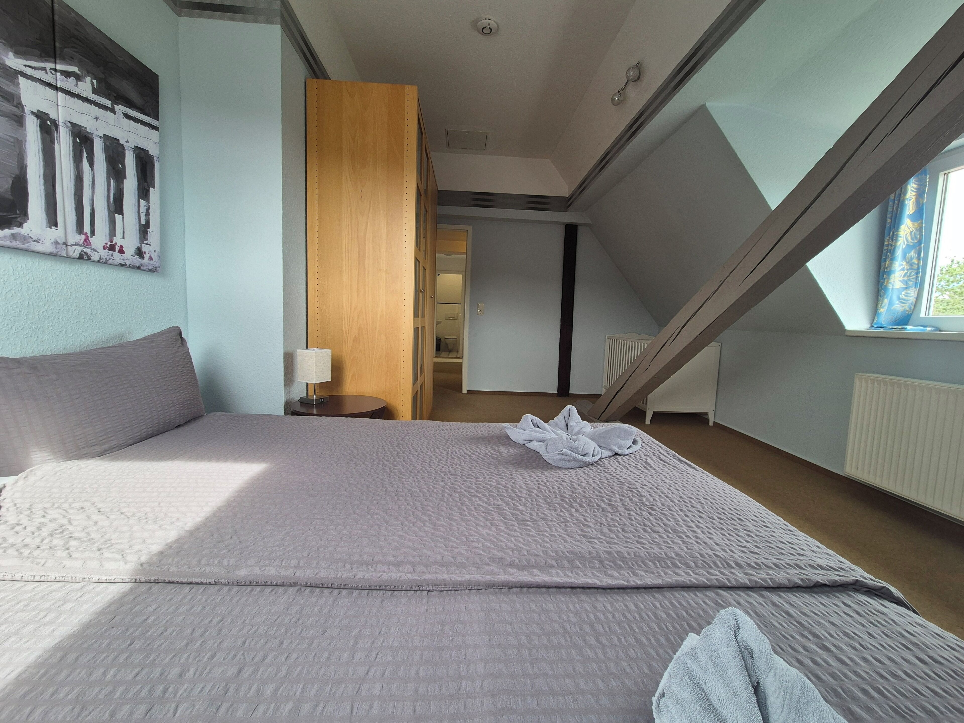 A bedroom with a large bed, a wooden panel wall, a window with a view, and a ceiling with a skylight.