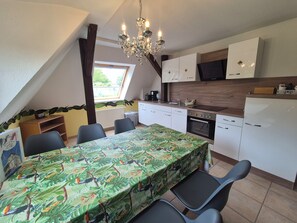 A kitchen with a dining table, chairs, a chandelier, and a window. - Apartments Villa Ratskopf (Wernigerode)