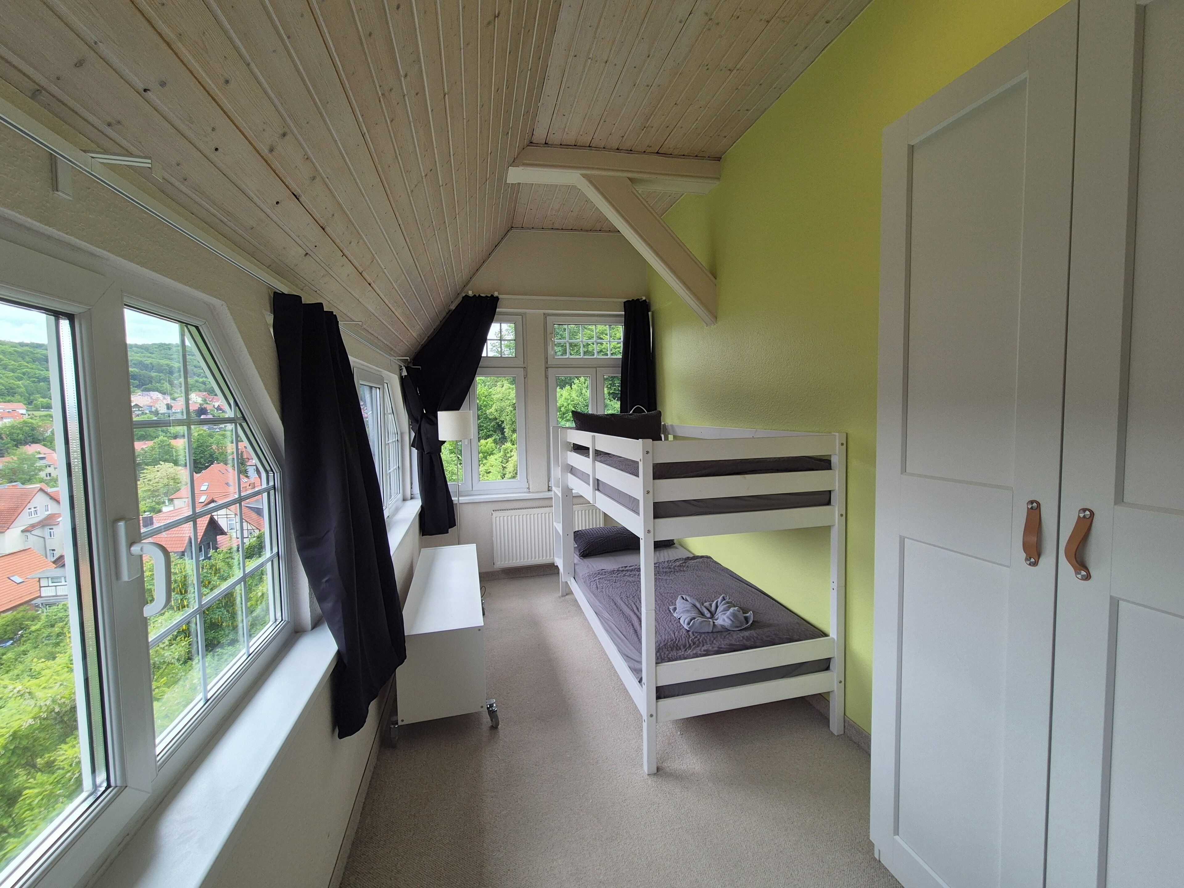 Een kamer met stapelbedden, een bureau en een raam met uitzicht op een woonwijk.