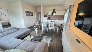 A modern living room with a grey sofa, a small coffee table, and a dining area with white chairs. - Apartments Villa Ratskopf (Wernigerode)