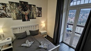 A bedroom with a large bed, two bedside tables, a nightstand, and a view of a balcony with a table and chairs. - Apartments Villa Ratskopf (Wernigerode)