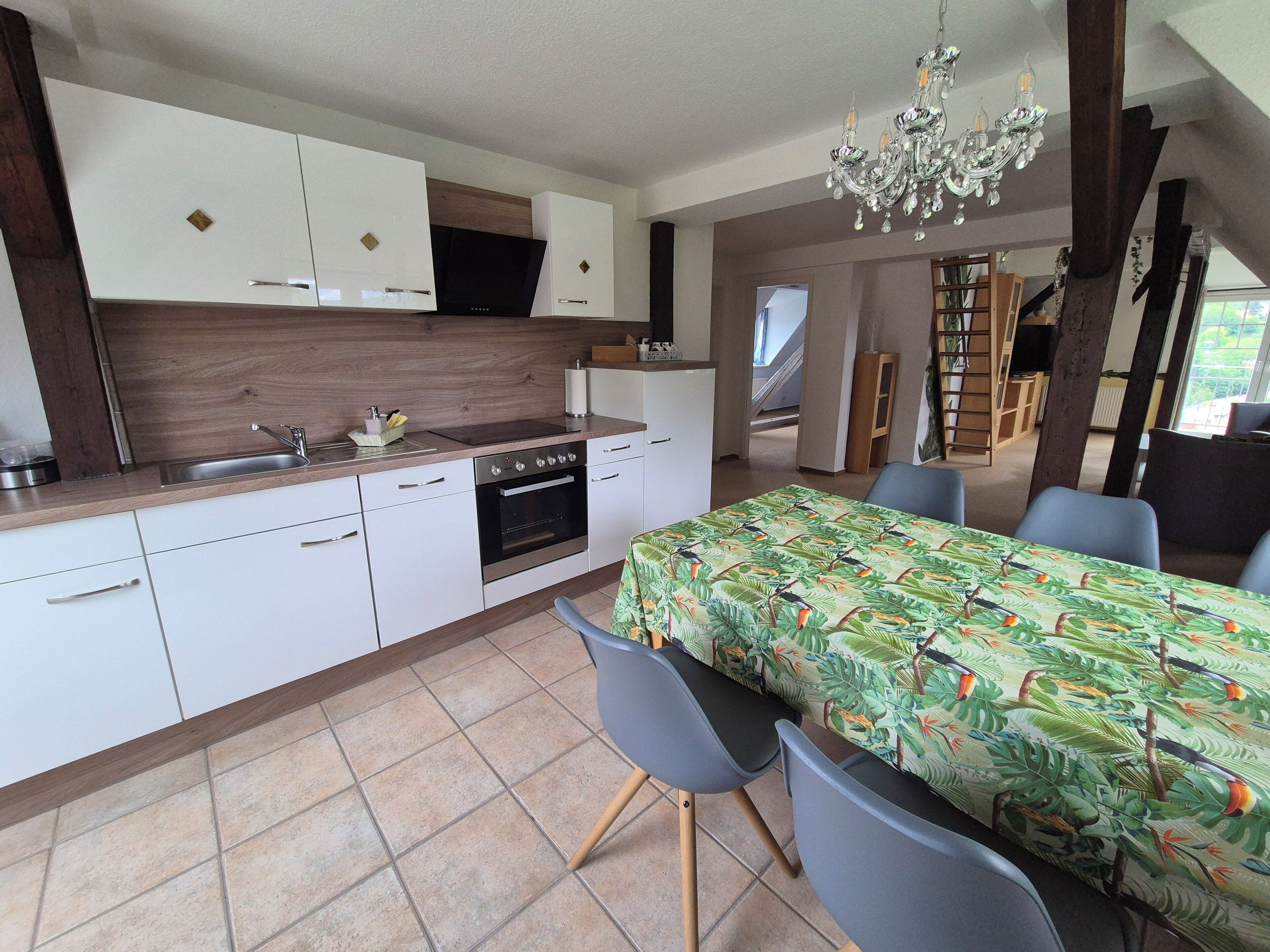A modern kitchen with white cabinets, a built-in oven, and a dining area with a table covered in a tropical print tablecloth.