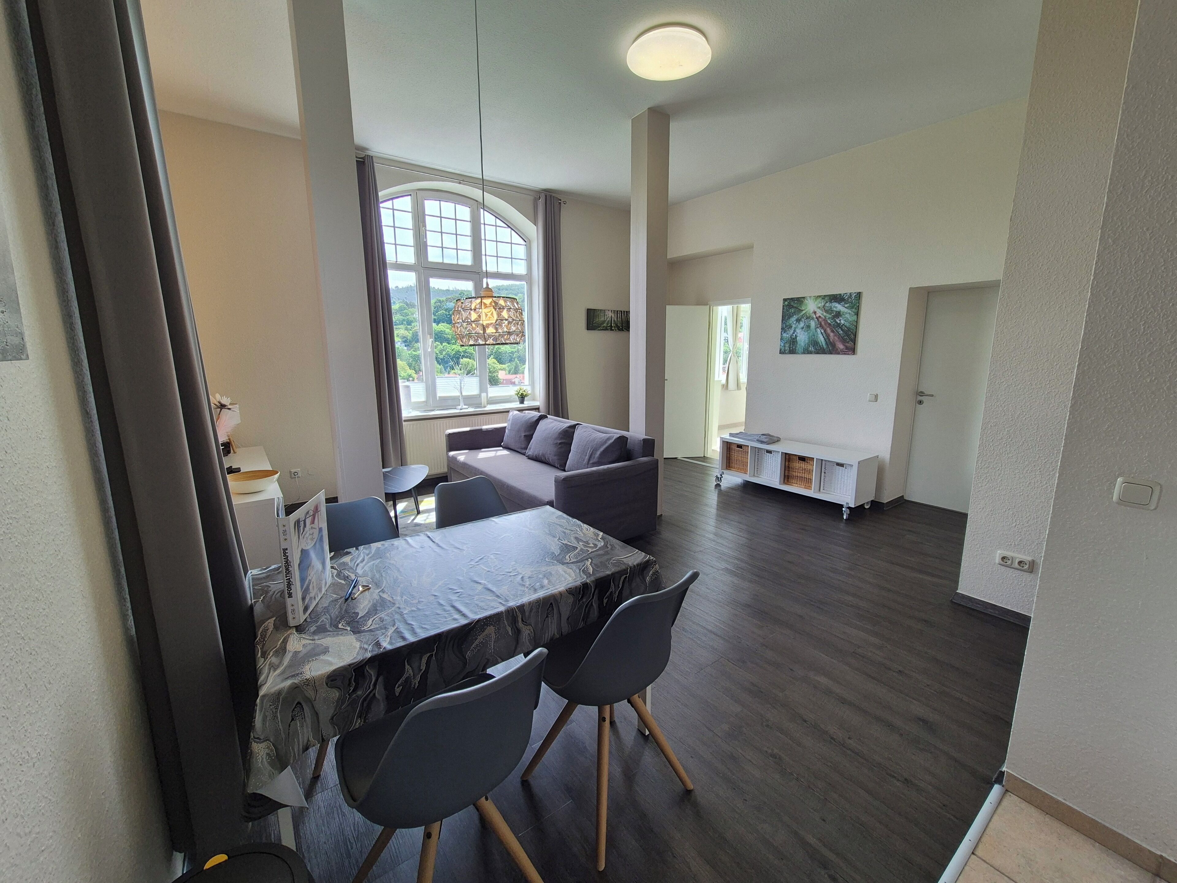 A spacious living area with a dining table, chairs, a sofa, and a large window with curtains.