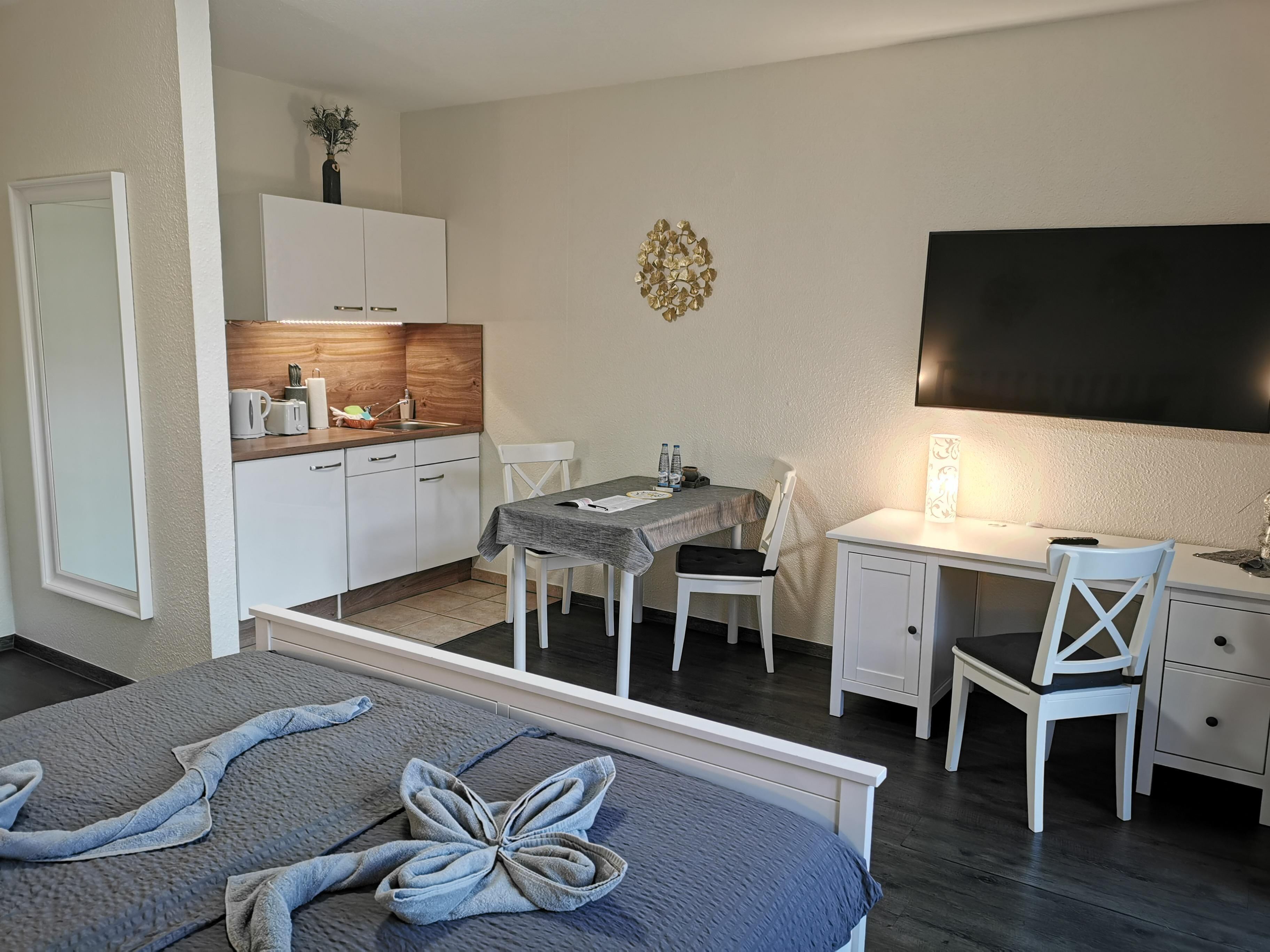 Une chambre d’hôtel de taille réduite, comprenant un lit, un bureau, une chaise, une petite kitchenette et un téléviseur.