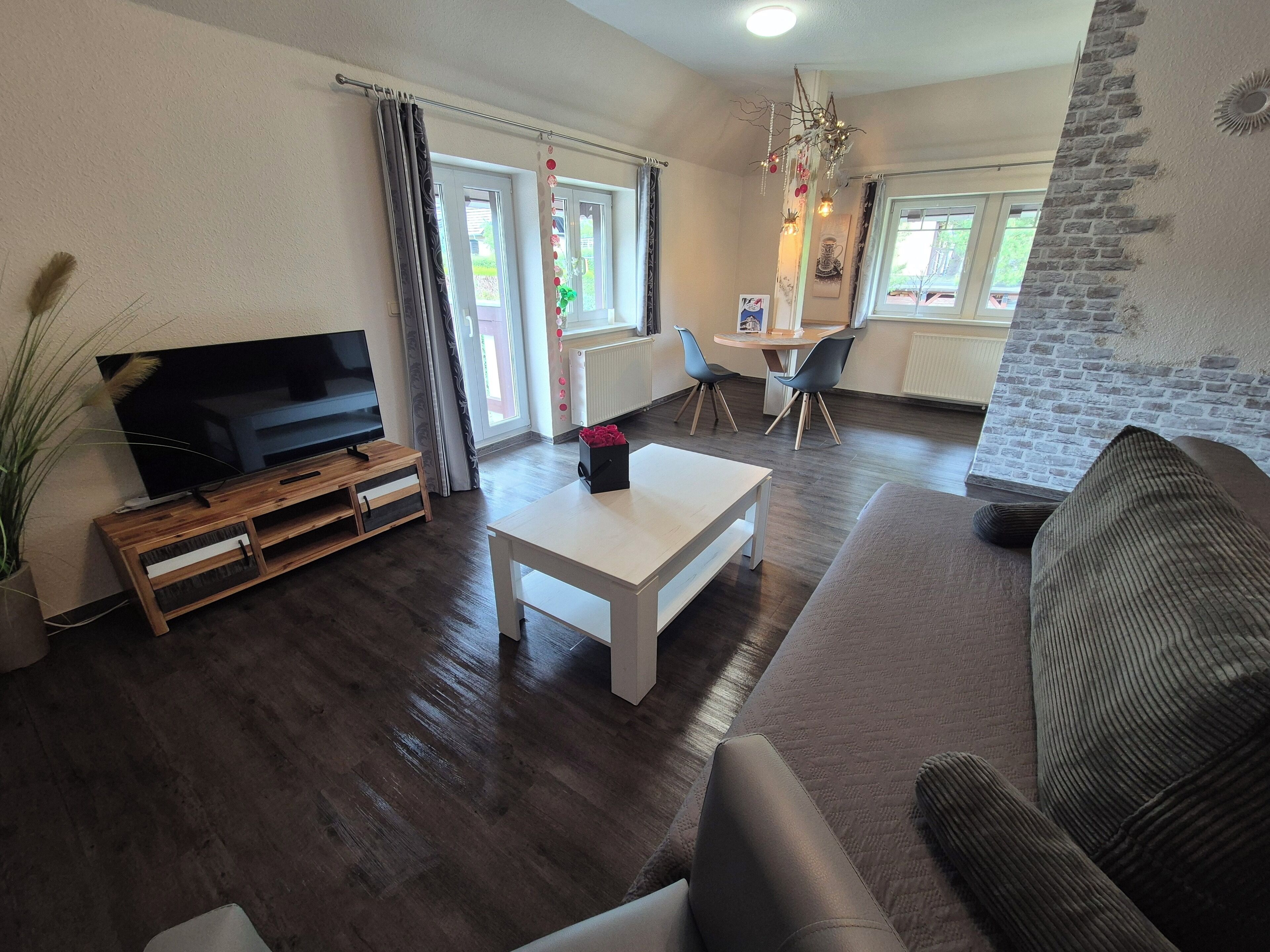 A living room with a flat-screen TV, a white coffee table, a sofa, and a dining area with two chairs.