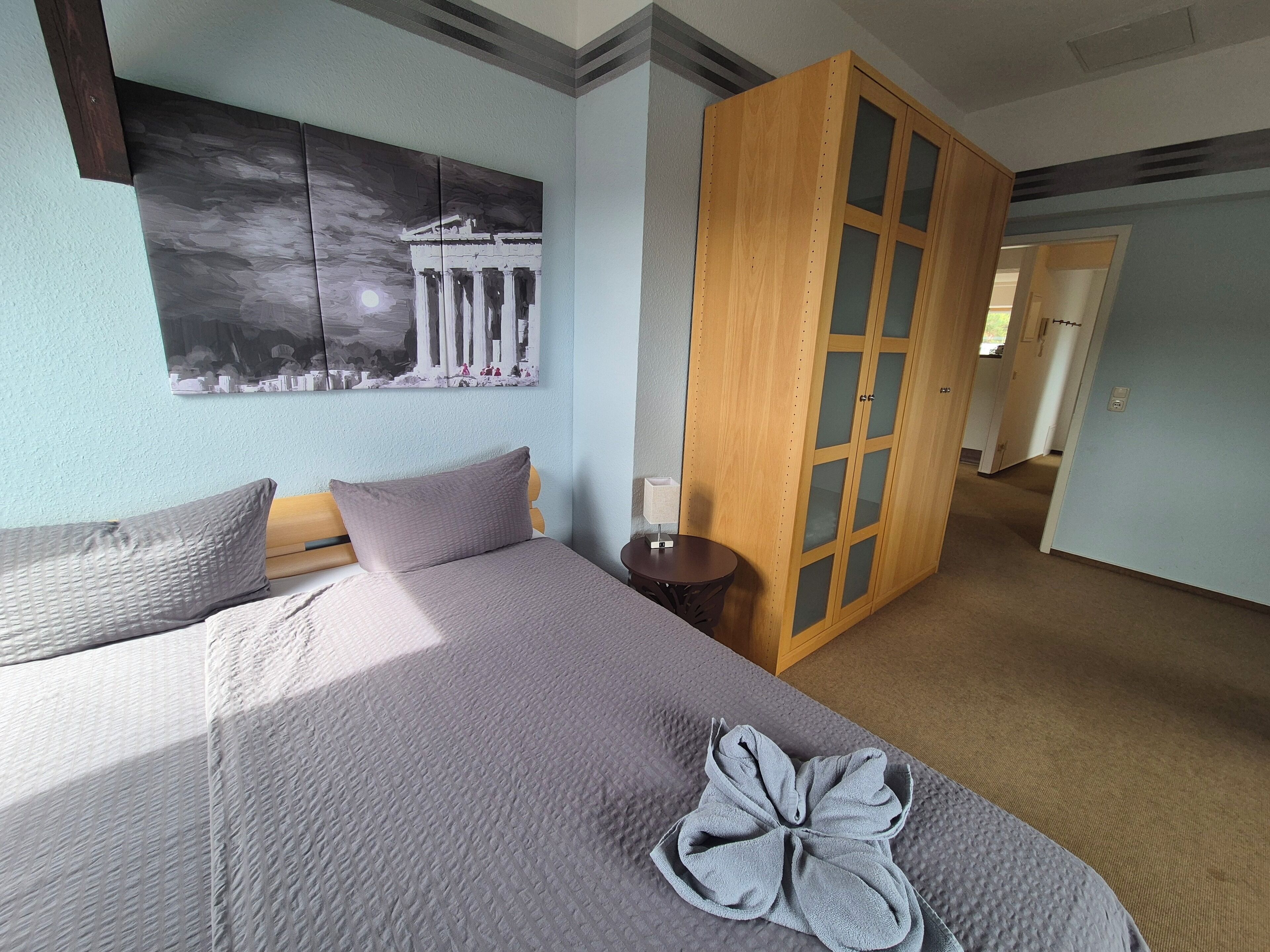 Une chambre d’hôtel avec un lit, une table de chevet, une armoire en bois et un tableau au mur.