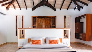 Un dormitorio con una cama grande, cabecera de madera, dos mesitas de noche con lámparas, una ventana con cortinas y un armario de madera.