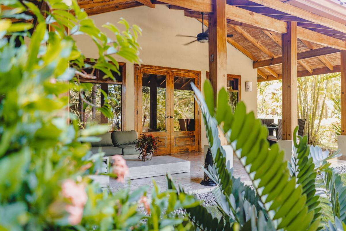 A covered outdoor area with wooden beams, a sofa, and a potted plant.