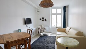 Una sala de estar con una mesa de comedor de madera, un sofá color beige, una mesa de centro redonda, una lámpara colgante de mimbre y un televisor montado en la pared.