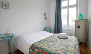 Un dormitorio con cama, mesita de noche, cómoda y ventana con cortinas.