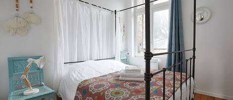 Una cama con dosel adornada con una colcha estampada, un dosel blanco, una silla azul y una mesita de noche con una lámpara.