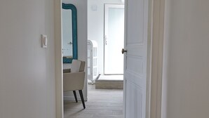 Un pasillo que lleva a un baño con puerta blanca, un espejo y una silla.