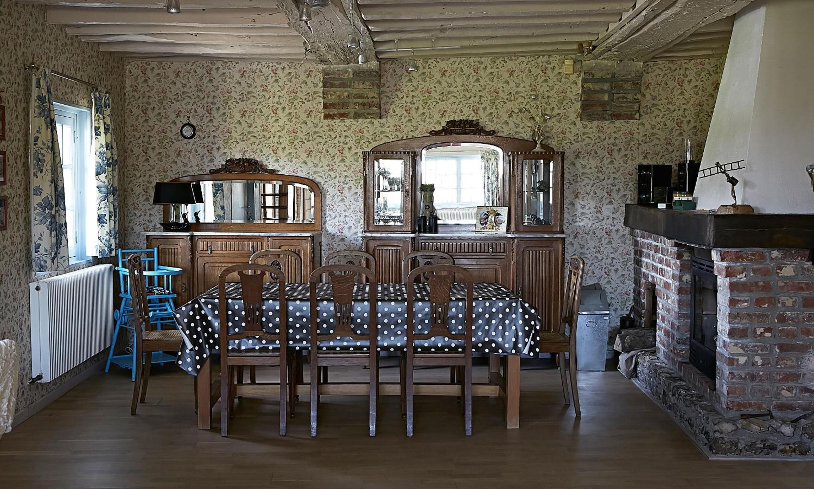 Un comedor con una mesa y sillas de madera, una silla azul, un aparador y una chimenea.