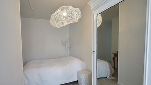 Un dormitorio con una cama, un taburete pequeño y una lámpara de techo con una textura original.