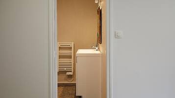 A narrow hallway leading to a bathroom with a white sink, a towel rack, and a radiator.