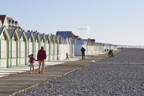 Un muelle de madera con casas de playa a un lado y una playa de guijarros al otro.