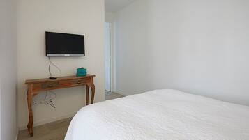 Une chambre à coucher avec un lit, un bureau en bois avec une télévision, et une porte donnant sur une autre pièce.
