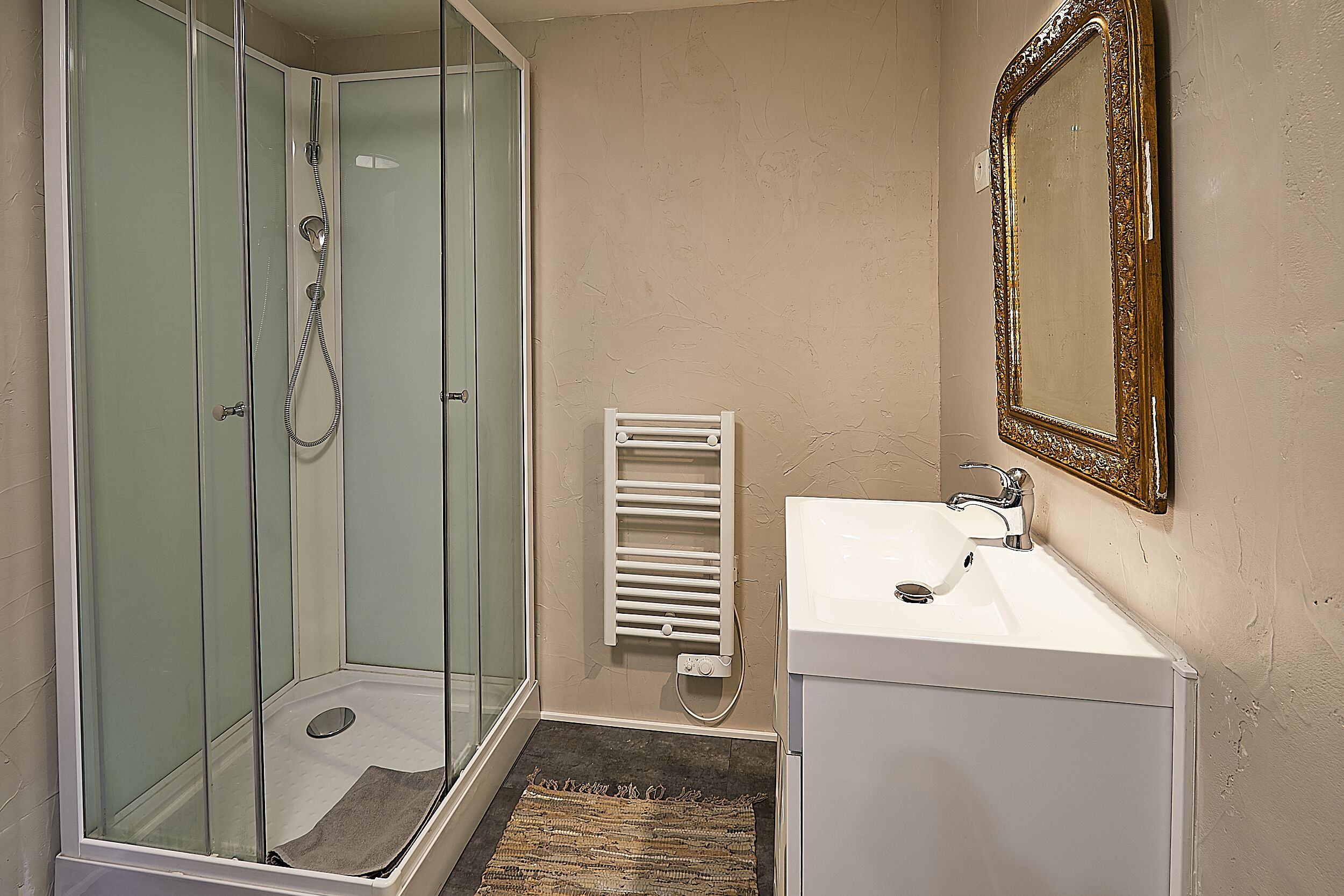 A bathroom with a glass-enclosed shower, a white sink, and a mirror with an ornate frame.