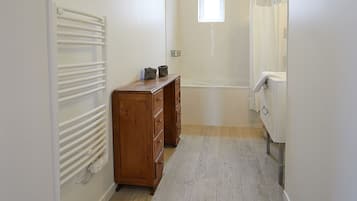A narrow hallway with a wooden dresser, a radiator, and a bathroom with a bathtub and shower.