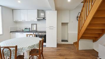 A modern kitchen with white cabinetry, a dining table with a polka dot tablecloth, and a wooden staircase.