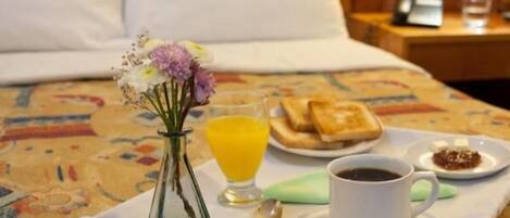 Een netjes opgemaakte ontbijttray op een bed, met een bloemenvaas, sinaasappelsap, toast, jam en een kop koffie.