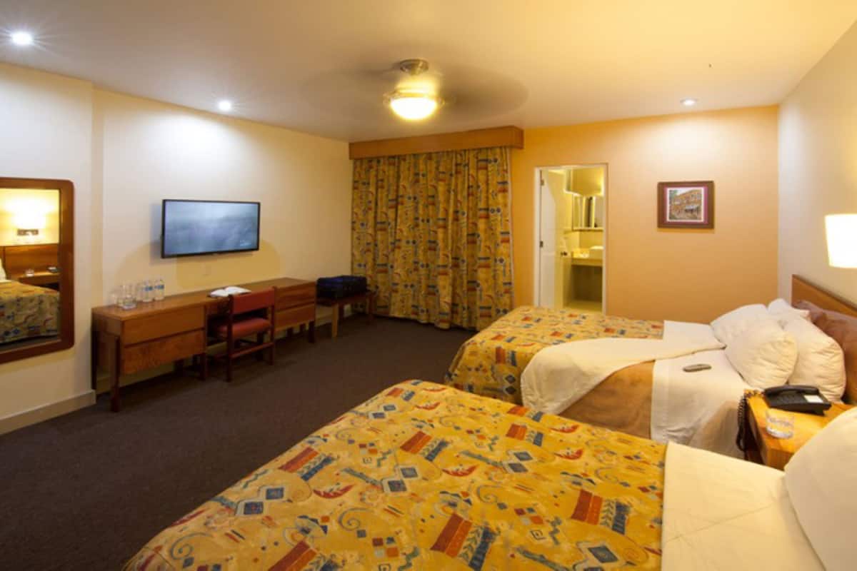 Ein Hotelzimmer mit zwei Betten, einem Schreibtisch, einem Sessel, einem Fernseher und einem durch eine offene Tür einsehbaren Badezimmer.