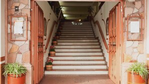 Una escalera de piedra que sube a un piso superior, con puertas de madera y macetas con plantas a los lados.