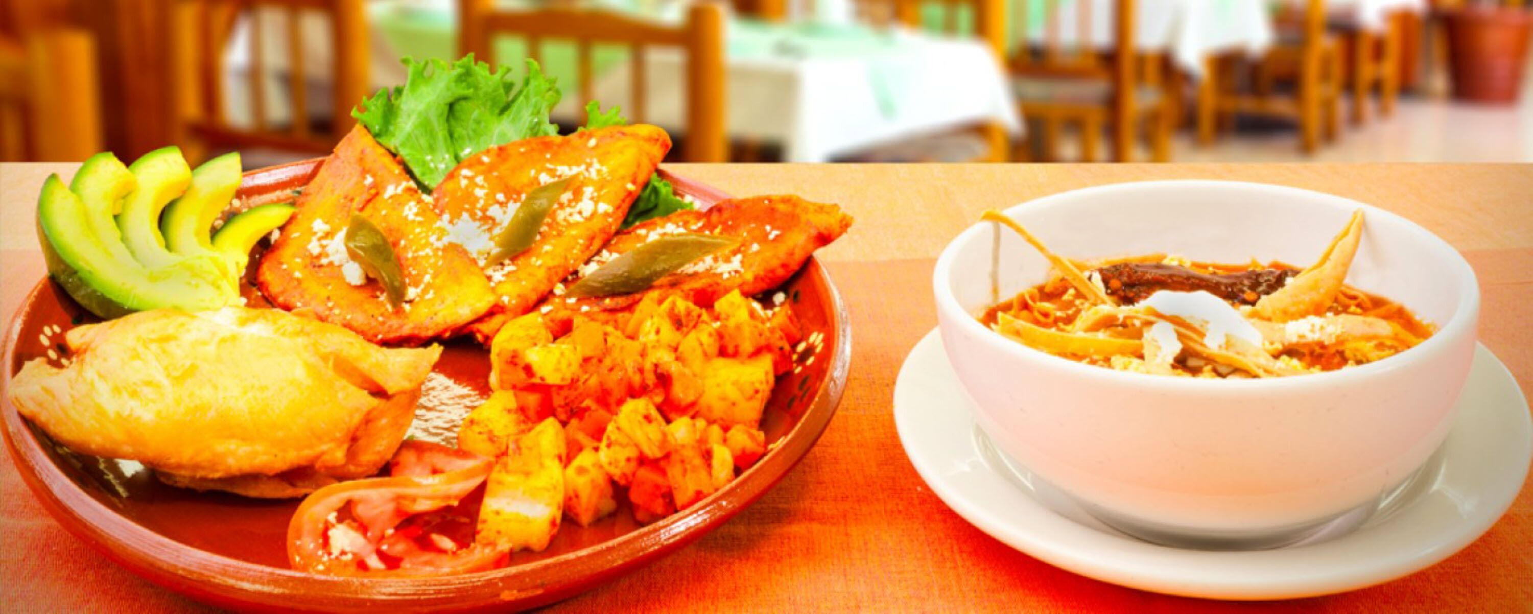 Una mesa con un plato de comida que incluye rodajas de aguacate, una preparación horneada y un tazón de sopa.
