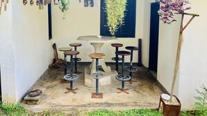 Un petit espace extérieur aménagé avec une table et des tabourets, entouré de plantes en pot et de plantes suspendues.