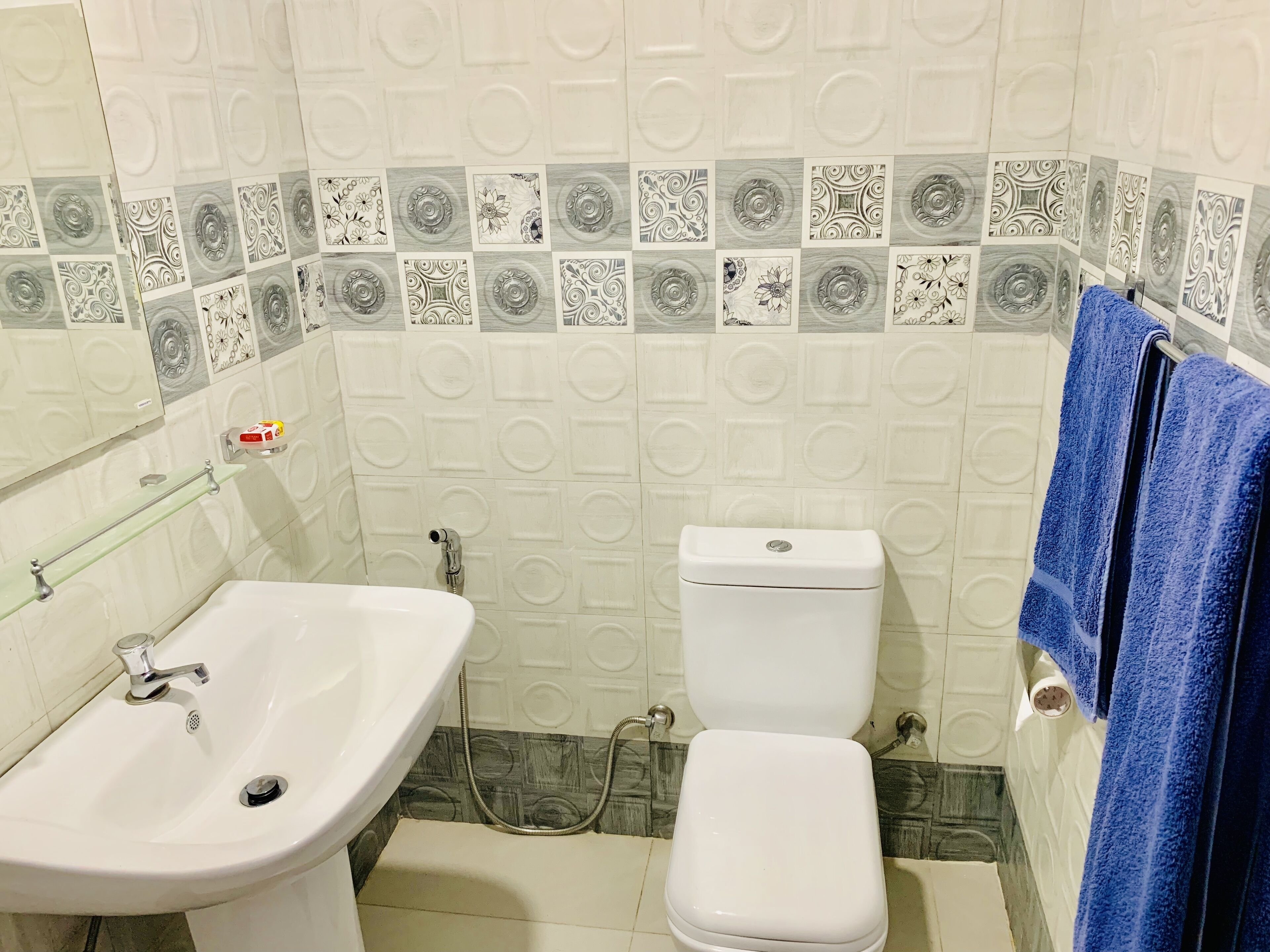 A bathroom with a white sink, toilet, and shower. The walls have patterned tiles.